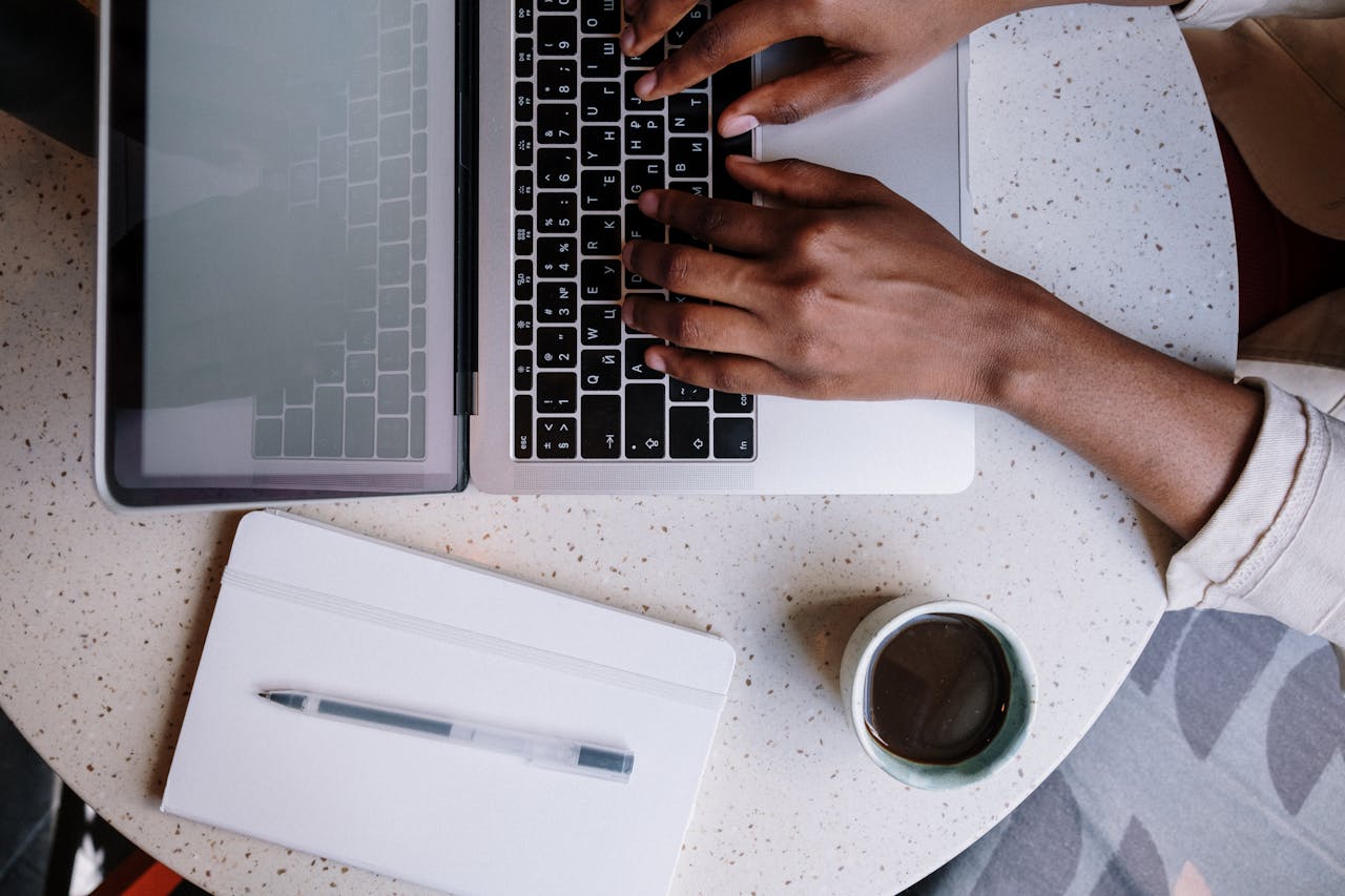 Top view of a person working on a laptop in a café with a notebook and coffee, ideal for business or blogging themes.